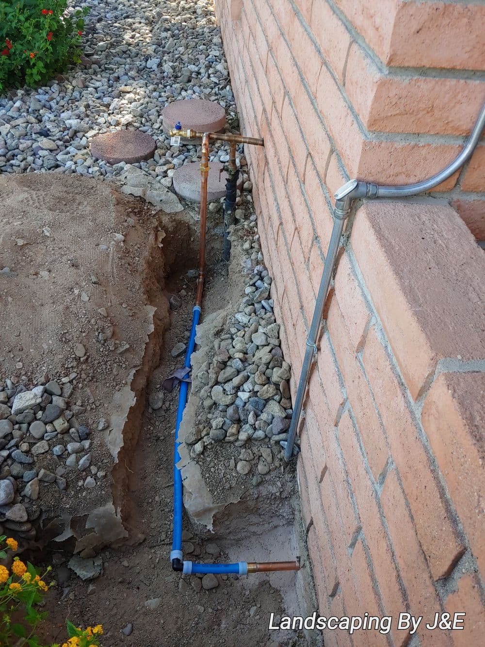 Pipes and landscaping elements beside a brick wall, showing excavation and installation.