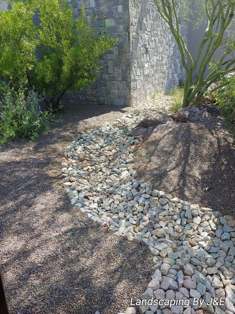 Desert landscape featuring a winding gravel path with stone accents and green shrubs.