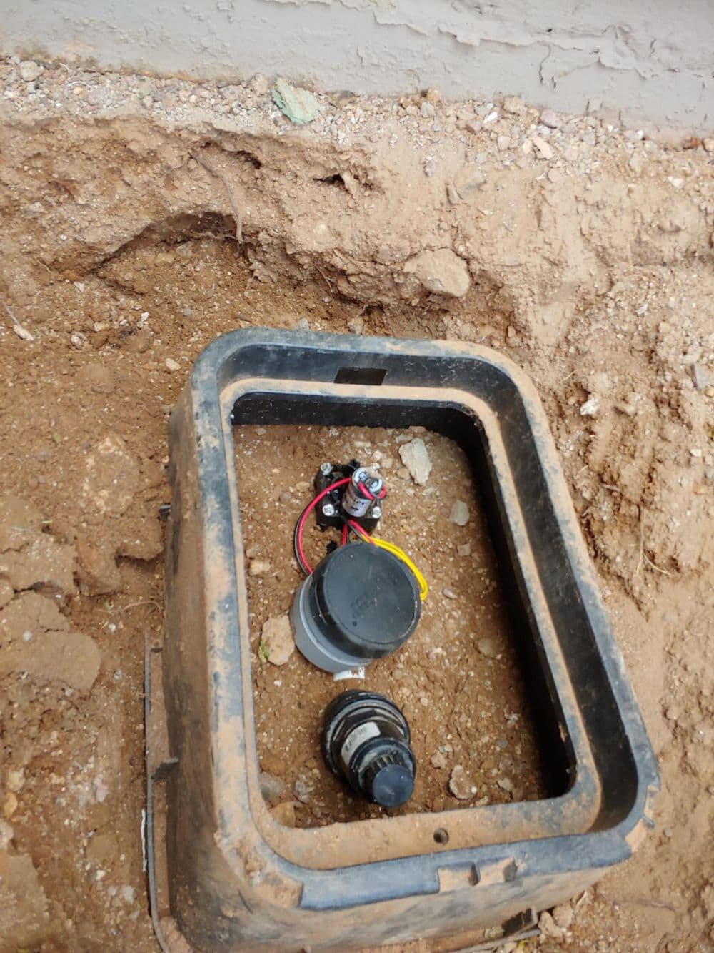 Underground valve box with wiring and components exposed in loose soil.