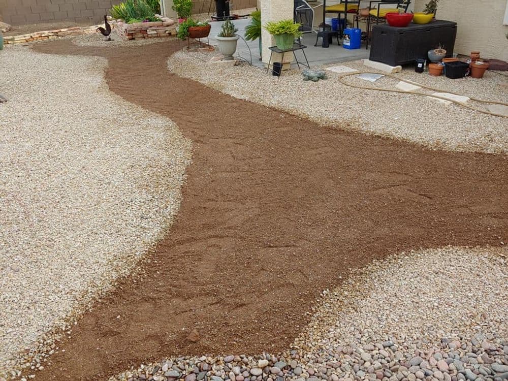 Landscaped gravel pathway in a garden with pots and furniture in the background.