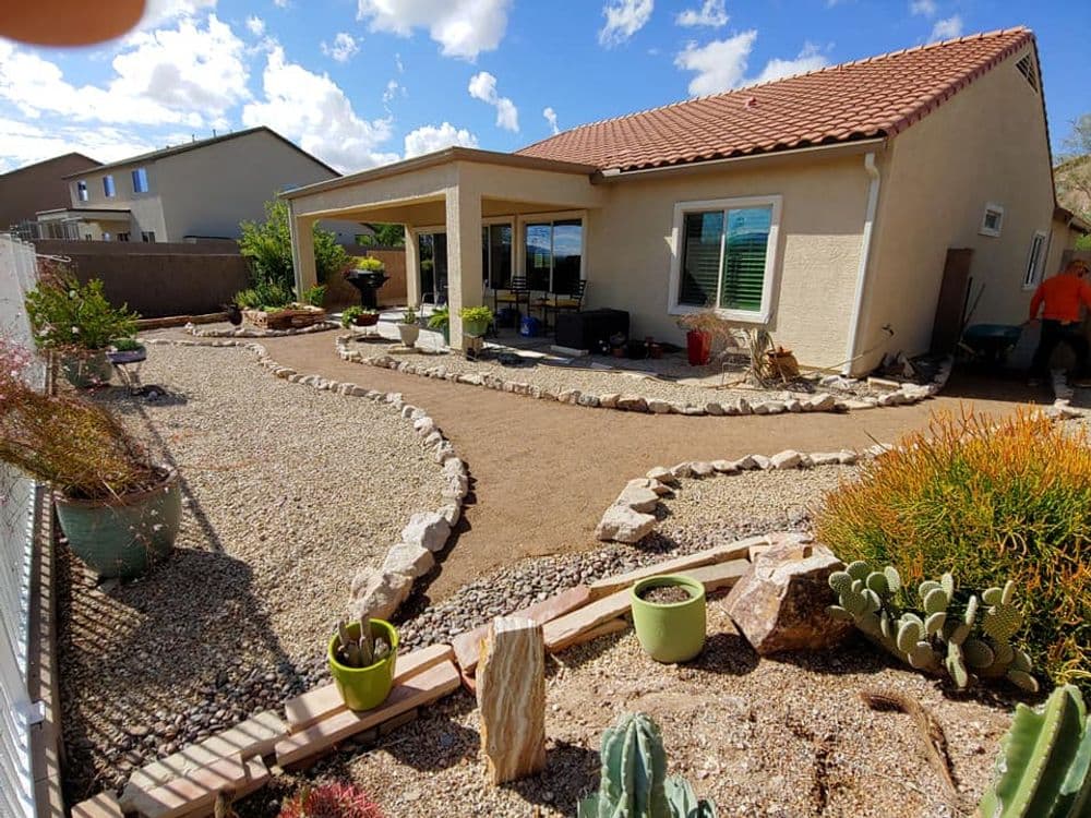 Desert landscape with a modern home, gravel path, and various potted plants.