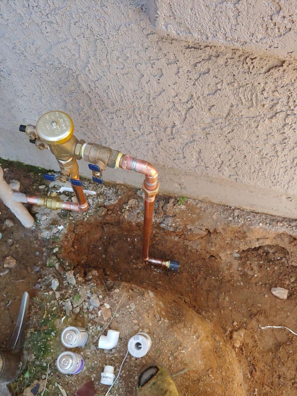 Newly installed copper plumbing with valves and fittings in a dirt trench.